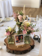 Soft jar displays including Roses, Wax Flower and Astilbe on a wood slice.  Floral design by Cotswold Blooms, wedding florist based in Cheltenham.