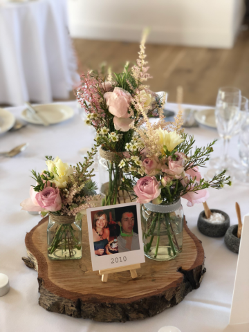 Soft jar displays including Roses, Wax Flower and Astilbe on a wood slice.  Floral design by Cotswold Blooms, wedding florist based in Cheltenham.