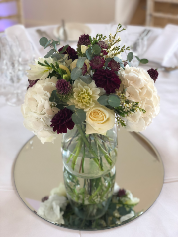 Burgundy Dahlia, Astrantia and Allium with white Hydrangea, Wax Flower and Roses sitting on a mirror plate. Floral design by Cotswold Blooms, wedding florist based in Cheltenham.