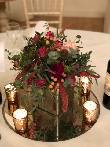 Raspberry and light pink display with warm copper tea lights. Floral design by Cotswold Blooms, wedding florist based in Cheltenham.