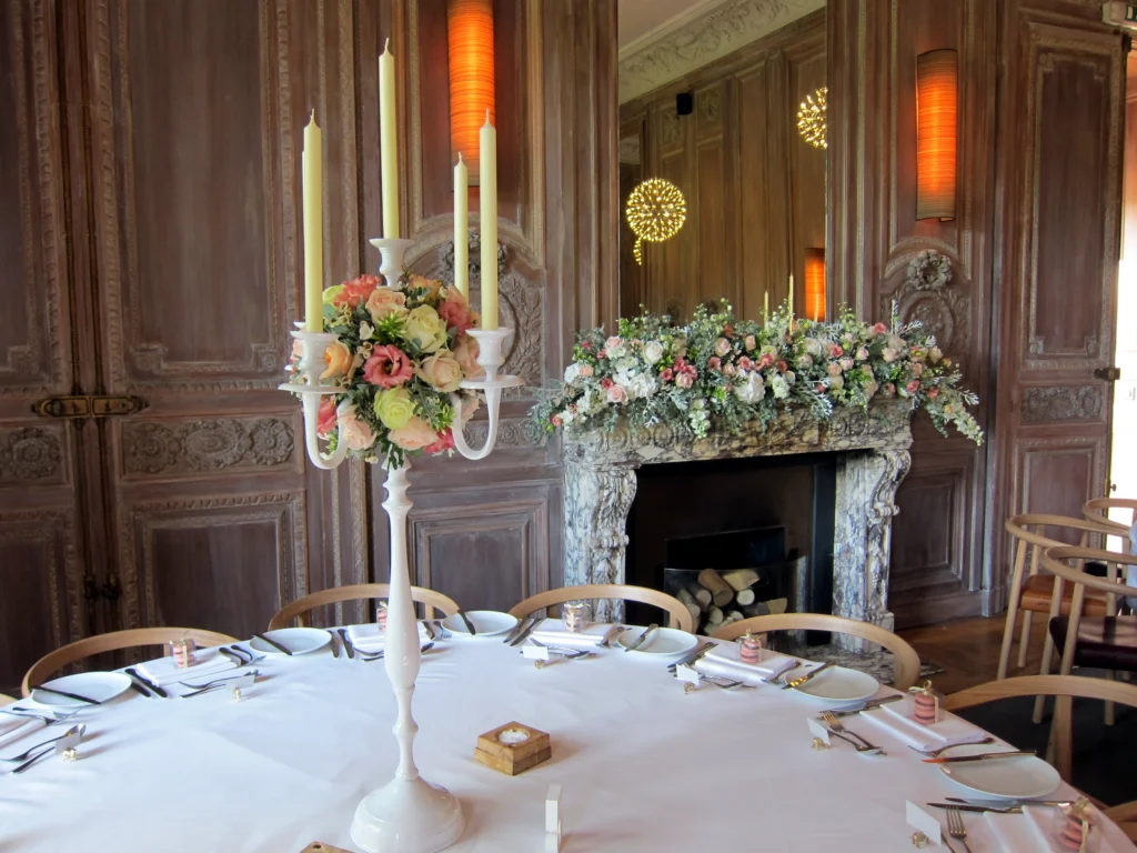 Elegant candelabra and fireplace floral arrangement with coral tones at Cowley Manor