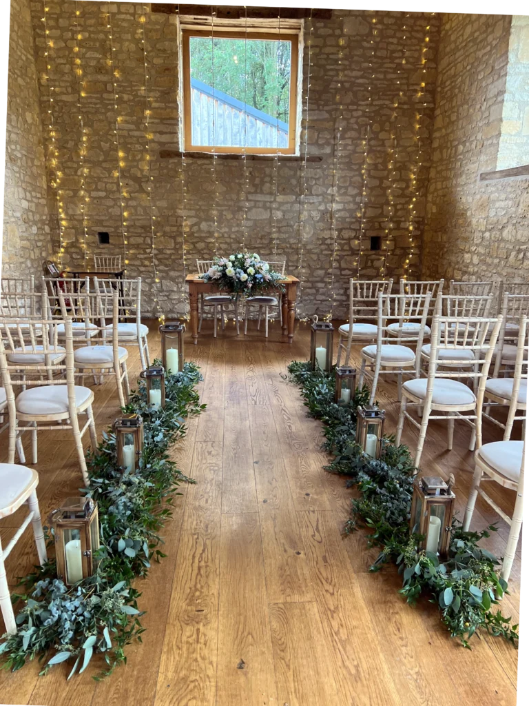 The Barn at Upcote wedding aisle featuring lush foliage and fairy light detailin