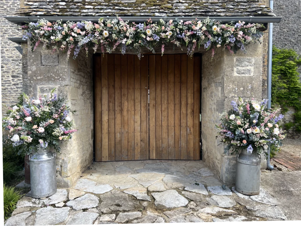 Rustic barn entrance with floral display over the door and milk churn arrangements at the sides
