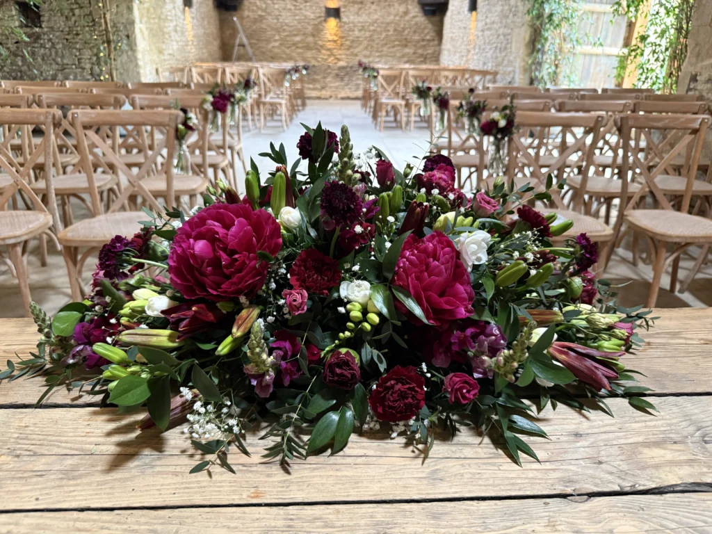 Burgundy long and low table display for ceremony front and top table at Stone Barn