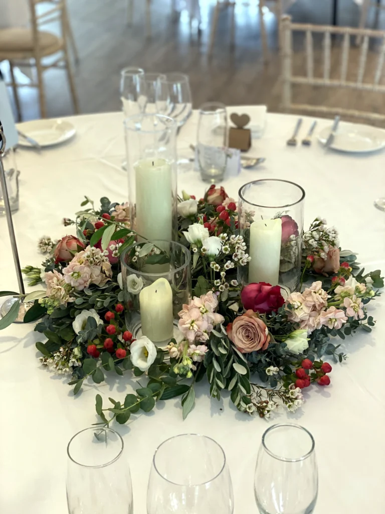Candle table display surrounded by roses, stocks and eucalyptus