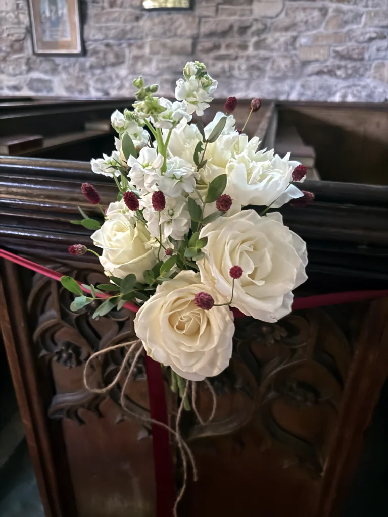 Rose pew end arrangement with rich burgundy floral detail