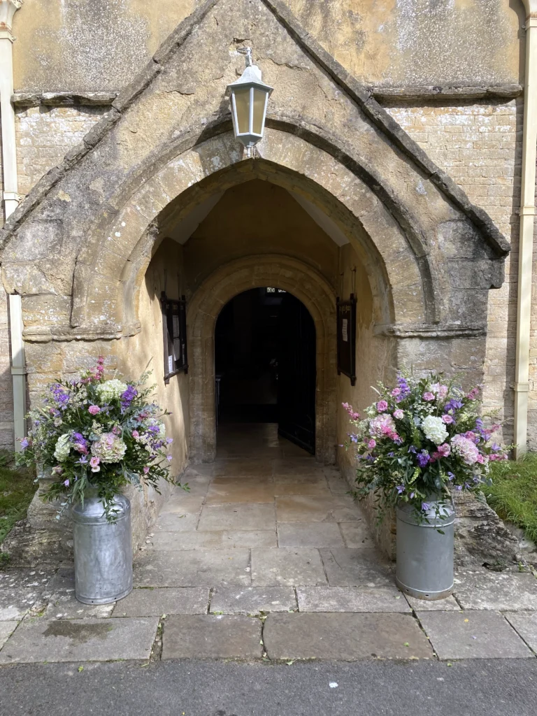 Purple and pink milk churn flower arrangements framing a church doorway