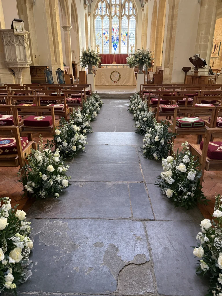 Traditional white and green church meadow displays with roses, delphinium, stocks and eustoma