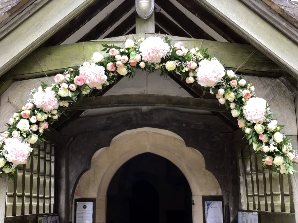 Light pink and white floral arch display with hydrangea, roses and ruscus greenery