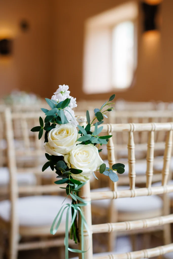 Wedding aisle marker featuring white roses, stock and greenery at Oxleaze Barn