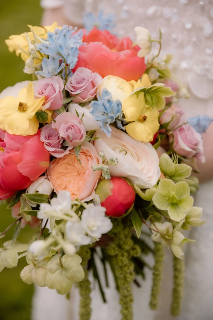 Boho bridal bouquet with peonies, ranunculus, hellebores and delphiniums in coral and yellow tones at Cowley Manor