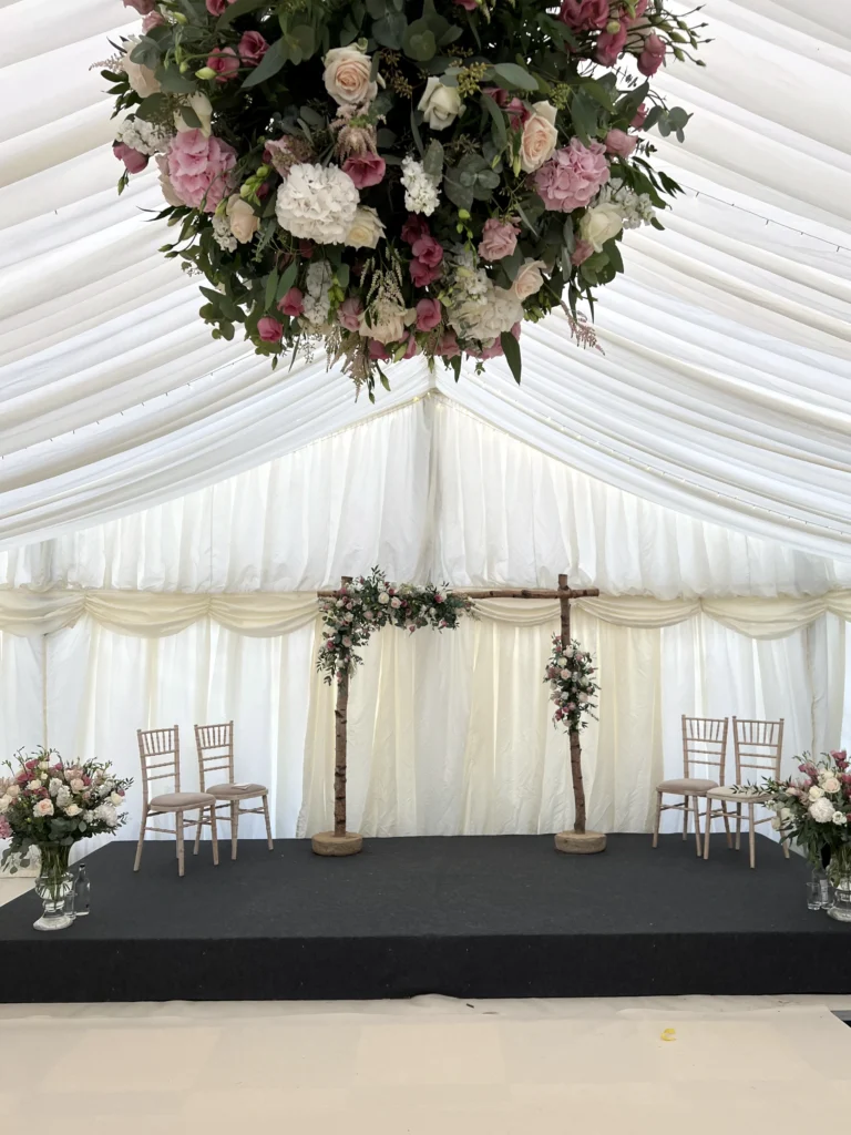 Hanging floral ball, asymmetric ceremony arch and glass urn displays inside a marquee wedding