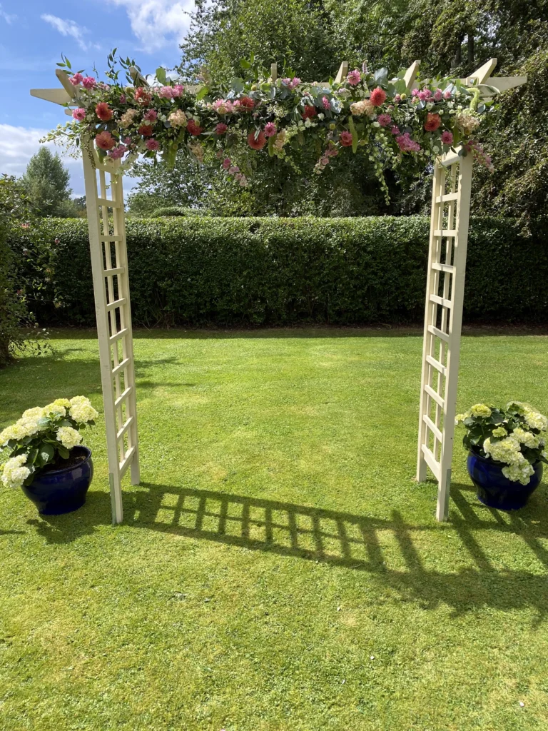 Vibrant seasonal flower arch for an outdoor marquee wedding ceremony in the Cotswolds