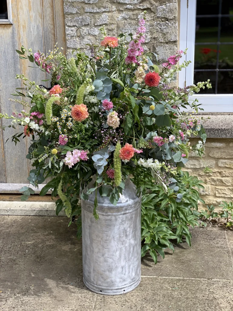 Boho milk churn floral displays dressed with seasonal flowers for a Cotswold marquee wedding