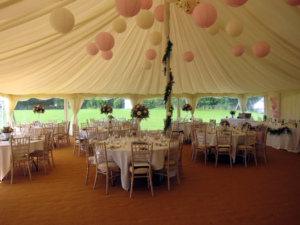 Martini vase wedding centrepieces with floral garlands wrapped around marquee poles at a Cotswolds wedding reception
