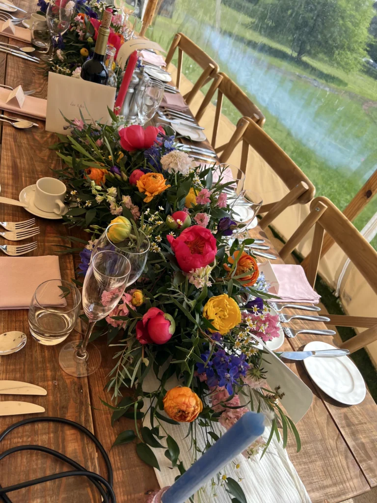 Bright and bold wedding table centrepiece featuring peonies and seasonal flowers at a Cotswolds wedding